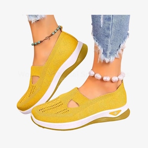 May include: Mustard yellow slip-on trainers with a breathable knit upper and a white sole. The shoes feature a cut-out detail on the side and a gold-coloured accent on the heel. Casual footwear.