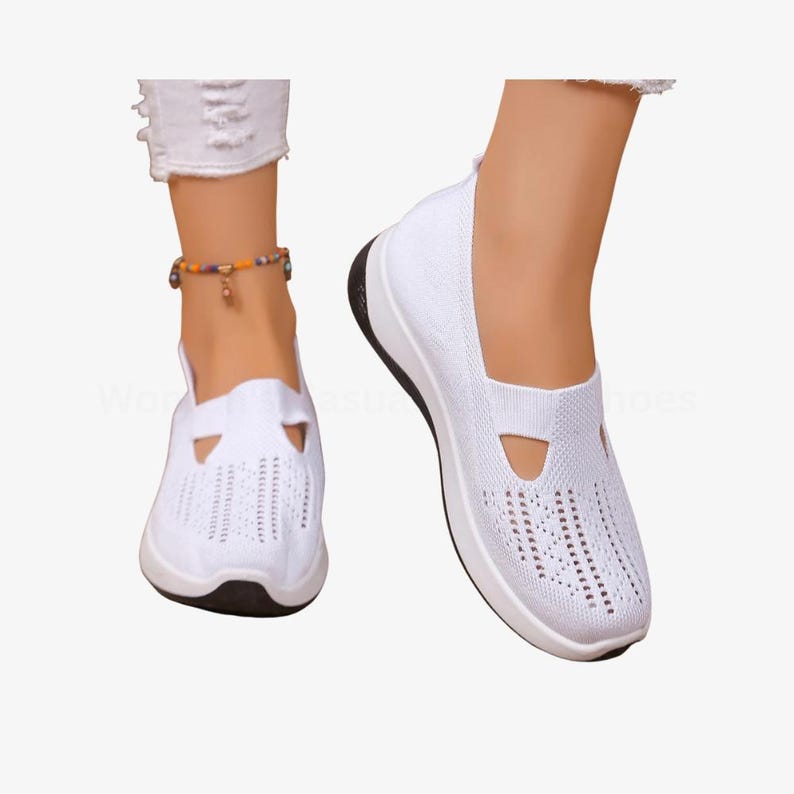 May include: White slip-on shoes with a breathable knit upper and a black sole. The shoes have a cutout detail on the top and are designed for casual wear. The shoes are shown on a person's feet.