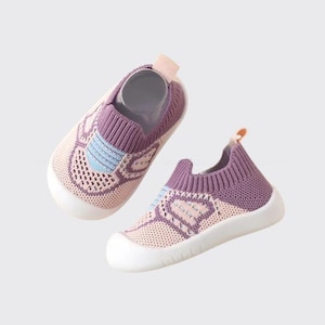 May include: A pair of baby shoes in a soft, pastel color palette. The shoes feature a breathable knit design in light pink and lavender, with blue accents. They have white soles and a pull tab at the heel.