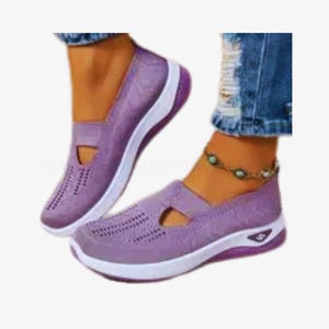 May include: Lavender slip-on shoes with white soles and purple trim. The shoes have a breathable, perforated design and a small cut-out detail. The shoes are shown on a person wearing blue jeans.