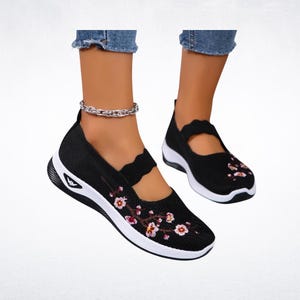Pu&ograve; includere: Scarpe nere slip-on con suole bianche e ricami floreali. Le scarpe hanno una tomaia in maglia traspirante e un cinturino decorativo. Il design include un piccolo logo bianco sul lato.