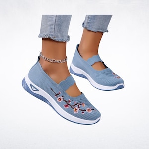 Pu&ograve; includere: Scarpe Mary Jane in mesh azzurro con suole bianche. Le scarpe presentano un ricamo floreale rosa e rosso. Hanno un cinturino smerlato e una suola bianca. Progettate per il comfort e lo stile.