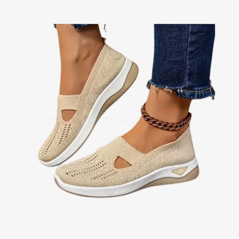 May include: Beige slip-on trainers with a breathable knit upper and white soles. The shoes have a cutout detail on the side and a textured design. The trainers are designed for casual wear.