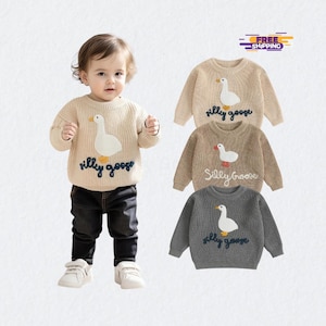 Könnte beinhalten: Beigefarbener Strickpullover mit weißer Gänseapplikation und dem Schriftzug "silly goose" in Blau. Der Pullover ist gerippt und hat lange Ärmel. Zusätzliche Pullover in Beige, Braun und Grau sind ebenfalls abgebildet.