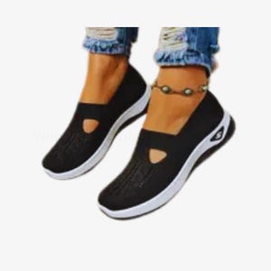 May include: A pair of black slip-on shoes with white soles. The shoes feature a breathable knit upper and a small, decorative cutout. The soles have a curved design with a small logo. These shoes are a comfortable and stylish choice for everyday wear.