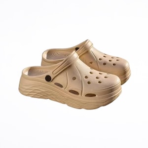 May include: A pair of beige clogs with a textured sole and multiple ventilation holes. The clogs have a strap that can be worn around the heel or folded forward. The shoes are made of a solid, lightweight material.