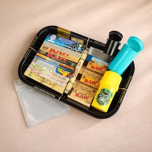 May include: A black rolling tray with various rolling papers, a clear plastic bag, and two plastic containers. The tray contains several packs of RAW and Elements rolling papers, and a yellow container with a gorilla graphic.