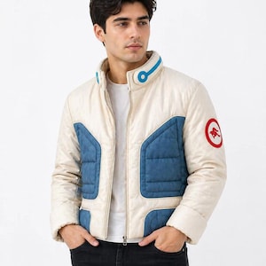 May include: Cream quilted jacket with blue panels and a red emblem. The jacket features a stand-up collar with blue detailing and a full-length zip. The jacket is a stylish outerwear option.