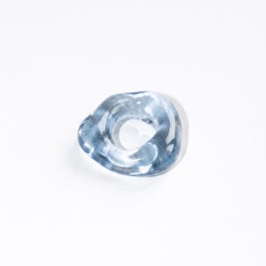 May include: A translucent, light blue ring with an irregular, organic, and wavy shape. The band has a smooth, glossy finish that catches the light, creating subtle variations in color depth and transparency throughout the circular form.
