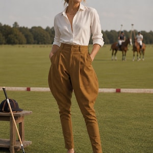 May include: A white long-sleeved button-down shirt paired with high-waisted tan jodhpurs featuring a pleated front and tapered legs. The outfit is completed with brown leather tassel loafers, creating a structured look suitable for equestrian activities.