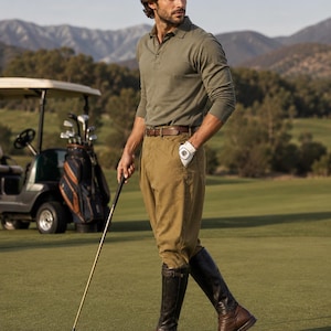 May include: An olive green long-sleeve polo shirt paired with tan trousers, a brown leather belt, and dark brown leather knee-high boots. The outfit includes a white golf glove and a golf club held in one hand on a green golf course.