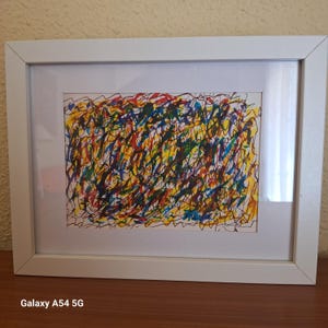 May include: Abstract art piece in a white frame. The artwork features a chaotic arrangement of colorful scribbles in red, yellow, blue, and green, creating a vibrant and energetic composition. The frame is rectangular and has a clean, minimalist design.