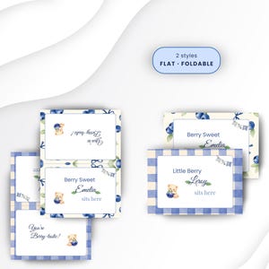 Könnte beinhalten: Rechteckige Platzkarten mit einem Aquarell-Motiv aus Blaubeeren und Teddybären sowie blauem Vichy-Karo-Rand. Der Text umfasst "Berry Sweet Emelia sits here", "Little Berry Leroy sits here" und "You're Berry-tastic!". Ein Etikett zeigt 2 Stile: FLAT und FOLDABLE.