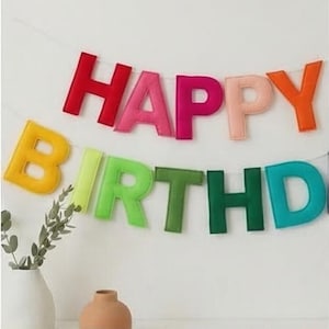 May include: A vibrant felt banner displaying "HAPPY BIRTHDAY" in a range of colours. The letters are red, pink, orange, yellow, green, and teal. The banner is strung on a white string, ideal for a birthday party.