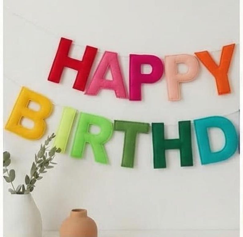 May include: A vibrant felt banner displaying "HAPPY BIRTHDAY" in a range of colours. The letters are red, pink, orange, yellow, green, and teal. The banner is strung on a white string, ideal for a birthday party.