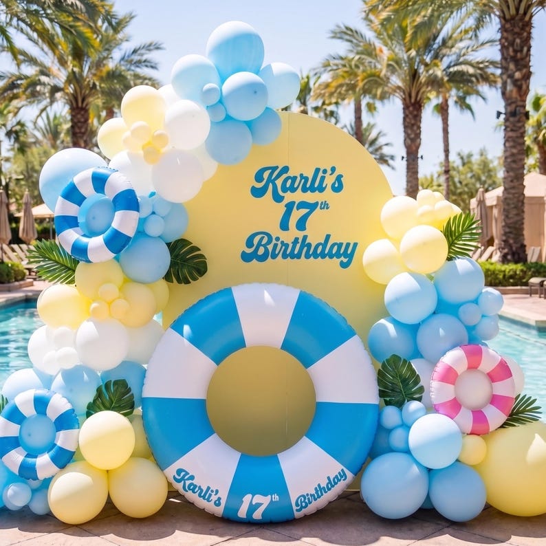 May include: A yellow arched backdrop with the text Karli's 17th Birthday in blue, decorated with blue, white, and yellow balloons, green palm leaves, and inflatable pool rings in blue and white stripes, plus one pink and white striped ring.