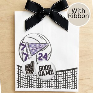 May include: White gift bag with a black bow and the text "With Ribbon." The bag features a volleyball graphic with a purple and white pennant that says "Wildcats" and the number 24. Two round buttons say "#1" and "GOOD GAME."