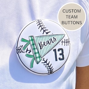 Peut inclure: Un bouton blanc sur le thème du baseball avec des détails de couture noirs. Le bouton présente un fanion vert et blanc avec le mot "Bears" et le numéro "13". Le texte "CUSTOM TEAM BUTTONS" est dans un cercle beige clair.