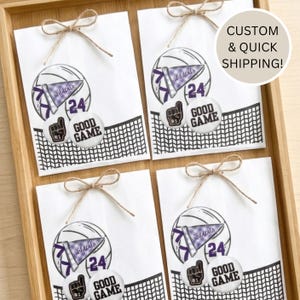 May include: Four white gift bags with a volleyball design, a pennant that says "wildcats", and the number "24". Each bag is tied with twine. The bags also have a "Good Game" button and a foam finger button.