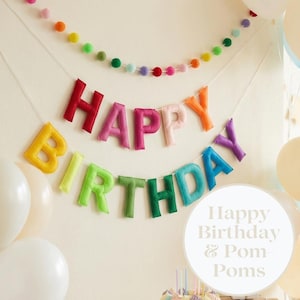 May include: A colourful 'HAPPY BIRTHDAY' banner made of felt letters, in shades of red, pink, orange, yellow, green, blue and purple. A string of multi-coloured pom-poms hangs above. White balloons are in the background. The image also includes the text "Happy Birthday & Pom Poms".