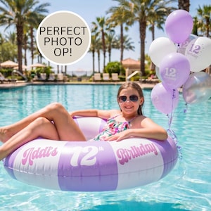 May include: A round inflatable pool float with alternating light purple and white stripes, featuring the text Addi's 12th Birthday. A cluster of purple, white, and silver balloons with the number 12 printed on them floats beside the pool ring.