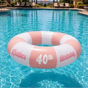 May include: A circular inflatable pool float featuring alternating pastel pink and white vertical stripes. The surface is printed with the white and pink text "Kristin's 40th Birthday" in a stylized, retro-inspired font across the front section.