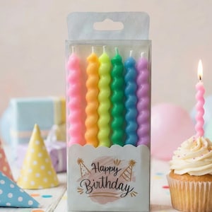 May include: A pack of seven rainbow-coloured spiral birthday candles. The candles are in shades of pink, orange, yellow, green, blue, and purple. The packaging features the words "Happy Birthday" and party hat illustrations. A lit pink candle sits on a cupcake.