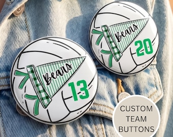 May include: Two white volleyball-themed buttons with a green and white pennant design that reads "Bears" and a number. One button has the number 13, and the other has the number 20. The buttons are on a denim jacket. The text "CUSTOM TEAM BUTTONS" is also visible.