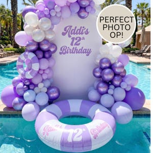 May include: A white rectangular backdrop with purple text reading Addi's 12th Birthday, surrounded by a balloon arch in shades of purple, lavender, and white. A matching purple and white striped inflatable pool float features the same birthday text.