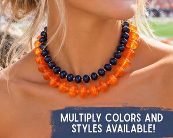 May include: A double-strand beaded necklace featuring one inner strand of dark navy blue beads and one outer strand of bright orange beads. The text on the image reads: MULTIPLY COLORS AND STYLES AVAILABLE!