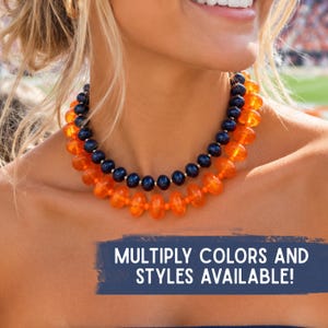 May include: A double-strand beaded necklace featuring one inner row of dark navy blue round beads and one outer row of translucent orange disc-shaped beads. The image includes the text: MULTIPLY COLORS AND STYLES AVAILABLE!