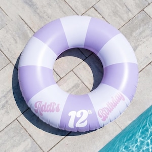 May include: An inflatable pool float featuring a circular design with alternating light purple and white segments. The surface is printed with the text Addi's 12th Birthday in a stylized white and light purple font across the bottom sections.