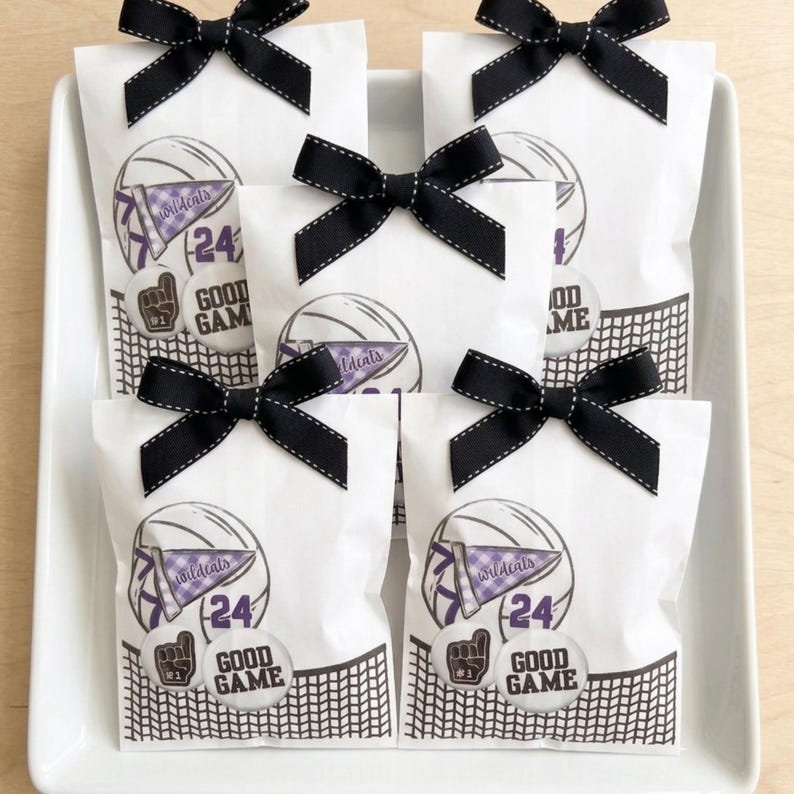 May include: White gift bags with black bows and stitching, arranged on a white tray. Each bag features a basketball graphic with the text "Wildcats", "24", and "Good Game". The bags are decorated with a black and white net design.