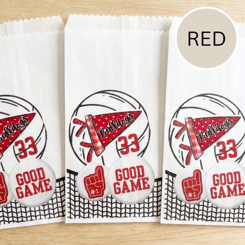 May include: White paper treat bags with a volleyball design. Each bag features a red pennant with "Bulldogs" and the number "33". Below, a button reads "GOOD GAME" and a foam finger. The word "RED" is in a circle.