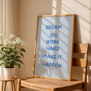 Puede incluir: Una lámina rectangular enmarcada con fondo azul claro y el texto azul "DREAM BIG WORK HARD MAKE IT HAPPEN" en una fuente apilada sin remates. El marco está hecho de madera de color claro y presenta un diseño sencillo y limpio.