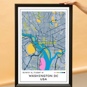 May include: A framed map print of Washington DC, USA, featuring a stylized street grid in shades of blue and grey with yellow and pink highlighted areas. The text 38.9073° N, 77.0369° W and WASHINGTON DC USA appears at the bottom of the print.