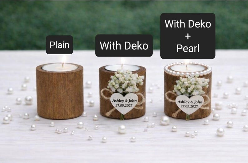 May include: Three wooden candle holders with lit candles. One is plain, one has a floral arrangement and a heart-shaped tag with text, and the third has pearls. The text on the tag reads "Ashley & John 27.05.2027".