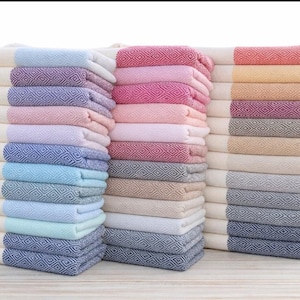 May include: Stacks of colorful, folded Turkish towels. The towels feature a diamond pattern and are in shades of blue, pink, and neutral tones. The towels are stacked neatly, ready for use.