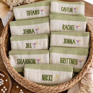 May include: A woven basket filled with personalized hand towels. Each towel is white with a green border and features an embroidered name and a cocktail glass. Names include Tiffany, Caitlin, Jenna, Rachel, Jill, Jenna, Shannon, Brittney, and Nikki.