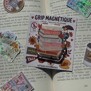 Può includere: Un supporto magnetico per telefono o tablet con una pila di libri etichettati Dragonfly Inn, Doose's Market, Luke's Diner, Miss Patty's, Kim's Antiques e Soda Shoppe, su un cartoncino bianco con la scritta GRIP MAGNÉTIQUE.