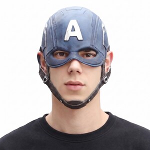 May include: A blue Captain America helmet with a white "A" on the forehead. The helmet has a chin strap and eye openings. The person in the image is wearing a black shirt.