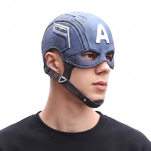 May include: A blue and silver Captain America helmet with the letter "A" on the forehead. The helmet has a chin strap and is worn by a person. The background is white.
