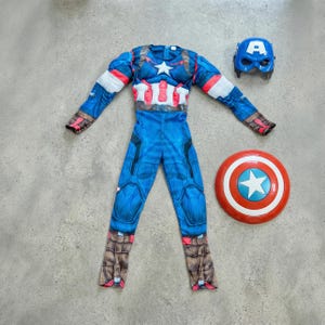 May include: A Captain America costume set, featuring a blue jumpsuit with a white star, red and white accents, and brown boot details. Includes a blue mask with a white "A" and a red, white, and blue shield. Perfect for cosplay or dress-up.