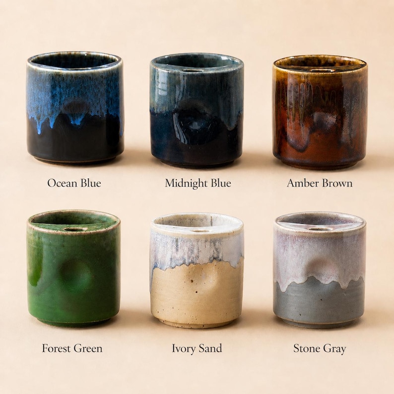 May include: Six ceramic toothbrush holders in various colors: Ocean Blue, Midnight Blue, Amber Brown, Forest Green, Ivory Sand, and Stone Gray. Each cylindrical holder has a slot for a toothbrush.