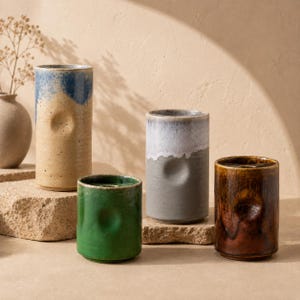 May include: Four ceramic vases in varying colors: blue and tan, gray and white, green, and brown. Each vase has a unique shape and texture, with a dimpled design on the side. The vases are displayed on a neutral surface.