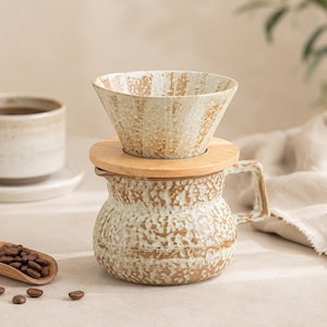 May include: A ceramic pour-over coffee maker with a wooden lid and a handle. The coffee maker is beige and brown with a textured surface. A wooden scoop with coffee beans and a cup are also visible.