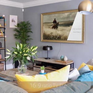 May include: A rectangular gold-toned TV frame featuring a 16:9 ratio smart object display area. The frame surrounds a landscape painting of a person riding a horse through a field. The frame is mounted on a gray wall above a wooden media console.