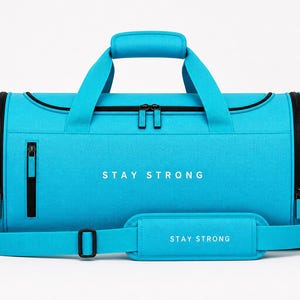 Könnte beinhalten: Eine türkisfarbene Sporttasche mit schwarzen Reißverschlüssen, Griffen und einem Schultergurt. Auf der Tasche steht in Weiß „STAY STRONG“ auf der Vorderseite und auf dem Schultergurt. Die Tasche ist für Sportausrüstung konzipiert.