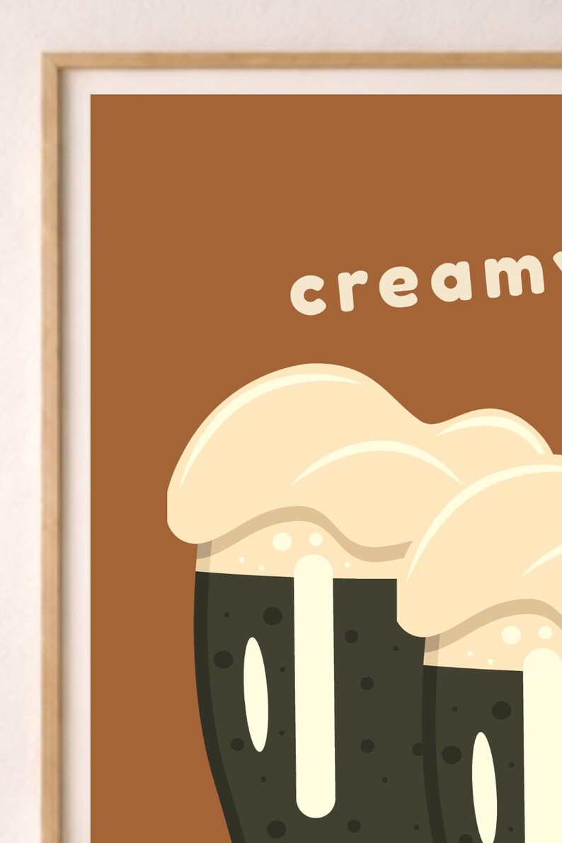 以下が含まれることがあります： 茶色の背景に白い文字で「creamy」と書かれた額装されたウォールアートプリント。イラストには、濃い茶色の液体が入った2つの濃い茶色のグラスが描かれており、その上には側面を滴り落ちる厚い薄ベージュ色の泡が乗っています。