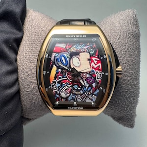 Puede incluir: Un reloj de pulsera Franck Muller Yachting con caja dorada en forma de tonel y correa de cuero negro. La esfera presenta una vibrante ilustración gráfica multicolor con formas abstractas y el texto Franck Muller y Yachting.